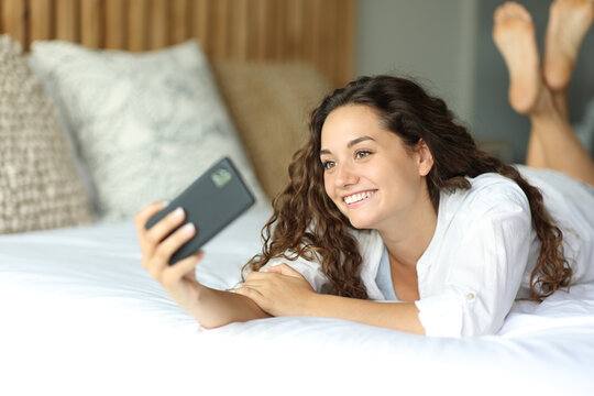 Happy woman on a bed taking selfie or recording with phone