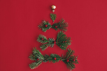 Modern Christmas tree, winter holidays concept. Stylish christmas tree made of fir branches, baubles, gold confetti on red background, festive flat lay. Creative idea. Merry Christmas!