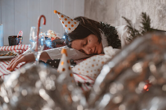 Woman in party hat sleeping peacefully on uncleaned festive table, resting after New Years Eve party