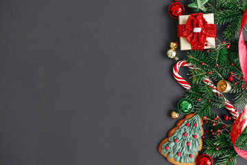 Modern christmas flat lay. Stylish christmas gift, tree branches, candy cane, festive decorations border on black background. Winter holidays banner. Merry Christmas and Happy Holidays