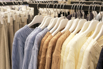 Multicolored knitted sweaters hanging on hangers in a female clothing store close-up.