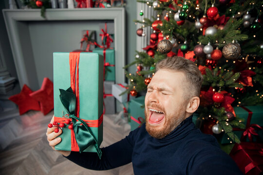 Young man is dissatisfied with Christmas gift box present, depicts frustration, crying, despondency, disappointment and screaming