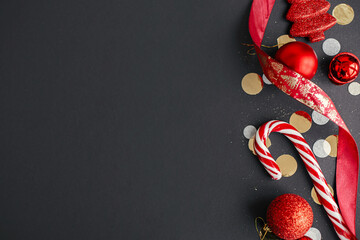 Modern christmas flat lay. Stylish christmas candy cane, confetti and red baubles border on black...