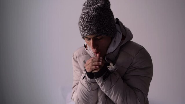 Unwell young man in hat and blanket stand in cold living room suffer from air conditioner lack. Unhealthy guy struggle from chill freeze at home. No heating
