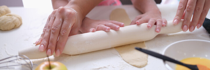 Mom and daughter roll out the dough with rolling pin in kitchen