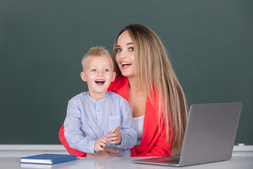 Little school child son using laptop with mother. Teacher tutor helping school child in class at school.