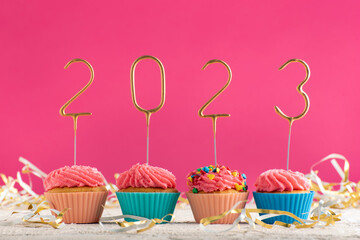 New Years background. Holiday cupcakes with numbers 2023 surrounded by New Years tinsel on pink background. Copy space.