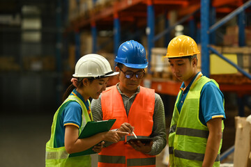 Middle aged male manager and young worker in hardhats and jackets using digital tablet for checking stock and order details