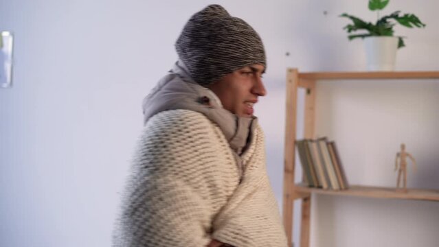 Ill young man feeling cold having flu grippe symptoms covered with blanket, sick guy shivering freezing at home, no heating problem and fever temperature