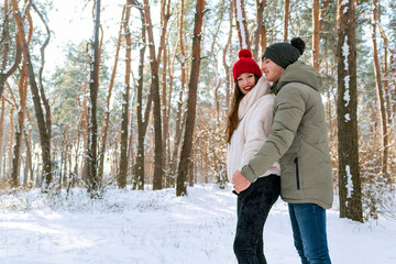 Young happy men and women are standing and hugging on sunny day in snow-covered park. Couple in a snowy winter park. Side view