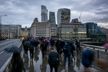 Blurred motion view of commuters with umbrellas in London going to work on a rainy, gray day in front of the city skyline during morning rush hour