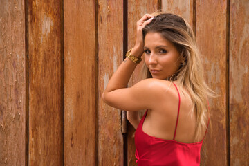 Fototapeta premium Portrait of young, attractive, blonde woman, wearing an elegant red party dress, with sensual look, on a background of wooden planks. Concept beauty, fashion, elegance, luxury, sensuality.