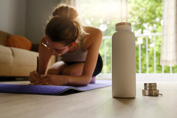 Side angle image of young caucasian woman making a journal entry while sitting on a yoga mat.