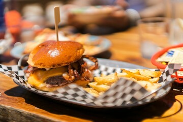 Soft focus of an appetizing burger with cheese and bacon served with fries on the side
