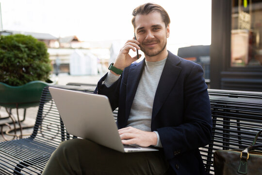 successful young male businessman working in the park on a laptop talking on a mobile phone
