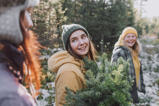 Smiling woman with spruce tree twigs looking at friend in forest