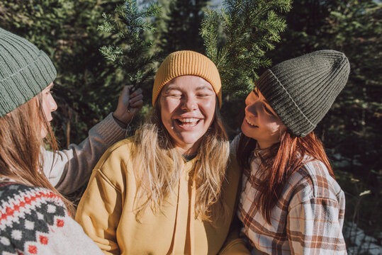 Happy women with twig of evergreen tree looking at friend in forest