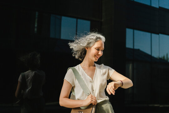 Smiling businesswoman with gray hair checking time in front of wall