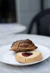 Classic Swedish shortbread cookie, known as hallongrotta, with jam in the middle and a cinnamon bun on a plate. Sweet pastry selection on plate on cafe table. Photo taken in Sweden.