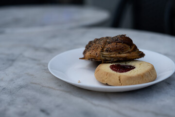 Traditional Swedish shortbread cookie, known as hallongrotta, with jam in the middle and a cinnamon bun on a plate. Sweet pastry selection on plate on cafe table. Photo taken in Sweden.