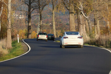 Kręta droga asfaltowa biegnie między drzewami jesienią.  - obrazy, fototapety, plakaty