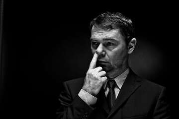 Mature man putting finger in nose against black background