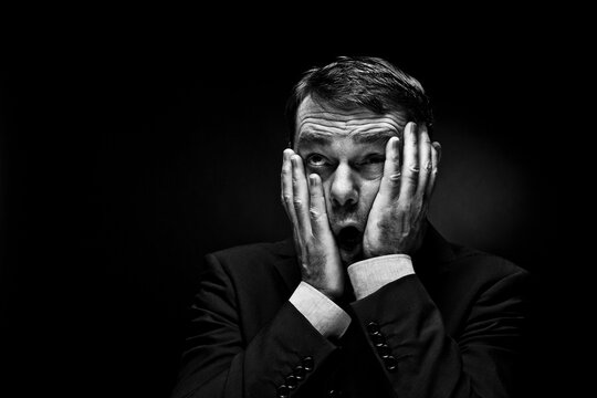 Mature man gesturing against black background, close up