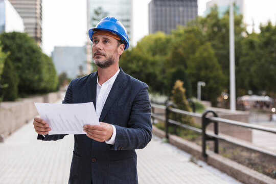 Engineer with hardhat holding chart on footpath