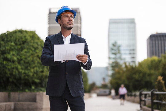Businessman with hardhat holding chart on footpath
