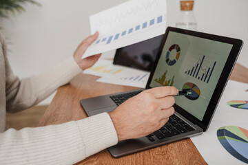 Businessman working on graphs and statistics over laptop at desk in office