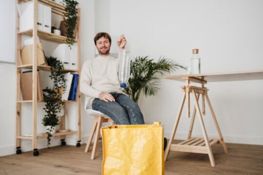 Businessman throwing plastic bottle into yellow bag at office