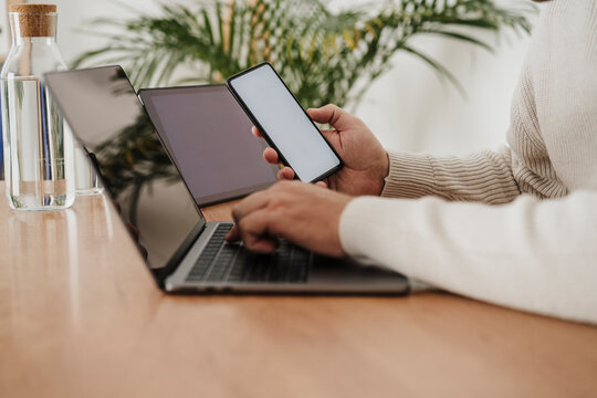 Hands of businessman using laptop and smart phone with blank screens at office