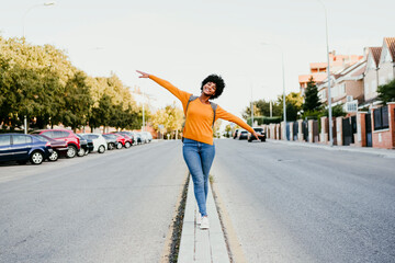 Happy young woman walking with arms outstretched on road