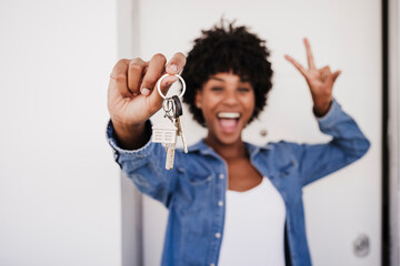 Cheerful woman showing house keys and peace sign gesture in front of door