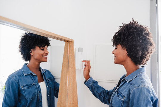 Happy young woman activating burglar alarm at home