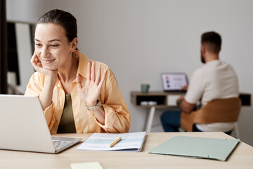 Young smiling student waving hand to tutor during online lesson or webinar while sitting in front of laptop screen at home