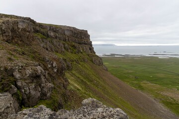 Lovely view of a tall rocky hill overlooking beautiful green hills under an overcast sky in Iceland