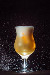 alcoholic cocktail in a glass container on the background of a black wall and drops of water
