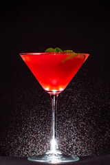 alcoholic cocktail in a glass container on the background of a black wall and drops of water