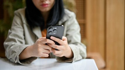 Tired and upset young Asian woman looking at her phone screen, waiting for a call