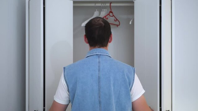 A young man opens an empty closet in search of clothes.