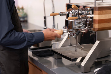 Hands of barista in dark blue uniform making coffee in bar.