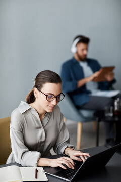 Young pretty student typing while sitting by desk in front of laptop and carrying out online task or searching for information