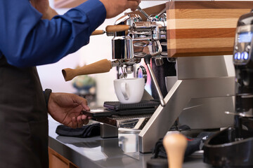 Professional coffee maker machine pouring fresh coffee into a white ceramic cup.