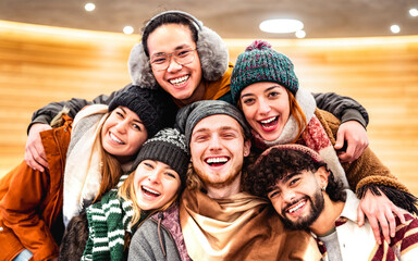 Happy multiracial guys and girls taking selfie on warm fashion clothes - Trendy life style concept with millenial people having fun together indoors on winter holidays - Warm bright filter - obrazy, fototapety, plakaty