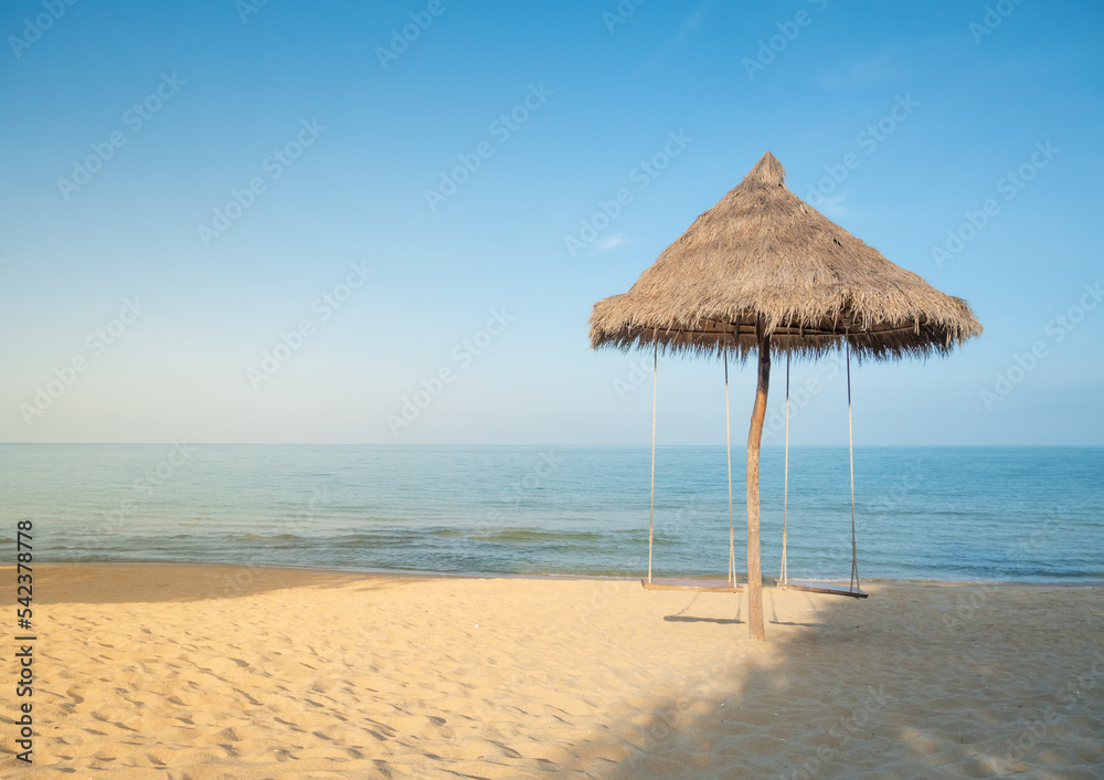 Wall mural The beach umbrella is made of natural grass with 2 swings hanging. There was a sea and blue sky in front.