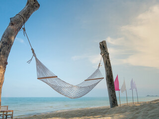classic hammock tied up wooden pillars On the sandy beach there is a blue sea, white and pink flags decorated around it looks beautiful. 