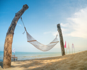 classic hammock tied up wooden pillars On the sandy beach there is a blue sea, white and pink flags decorated around it looks beautiful. and there is a bamboo chair in front