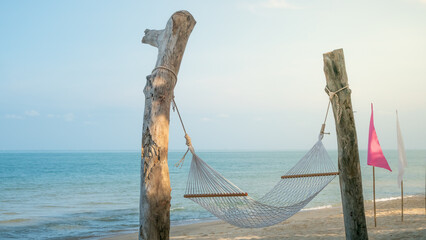 classic hammock tied up wooden pillars On the sandy beach there is a blue sea, white and pink flags decorated around it looks beautiful. 