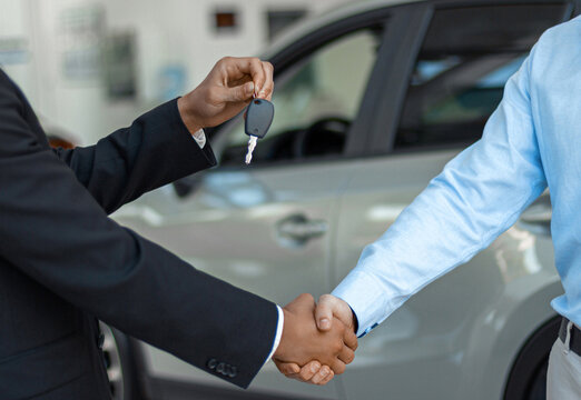 Close up of consultant giving car key to buyer after successful deal in auto show